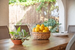 Un tavolo di legno con un cesto di limoni intrecciato, una pianta in vaso e un piatto bianco.