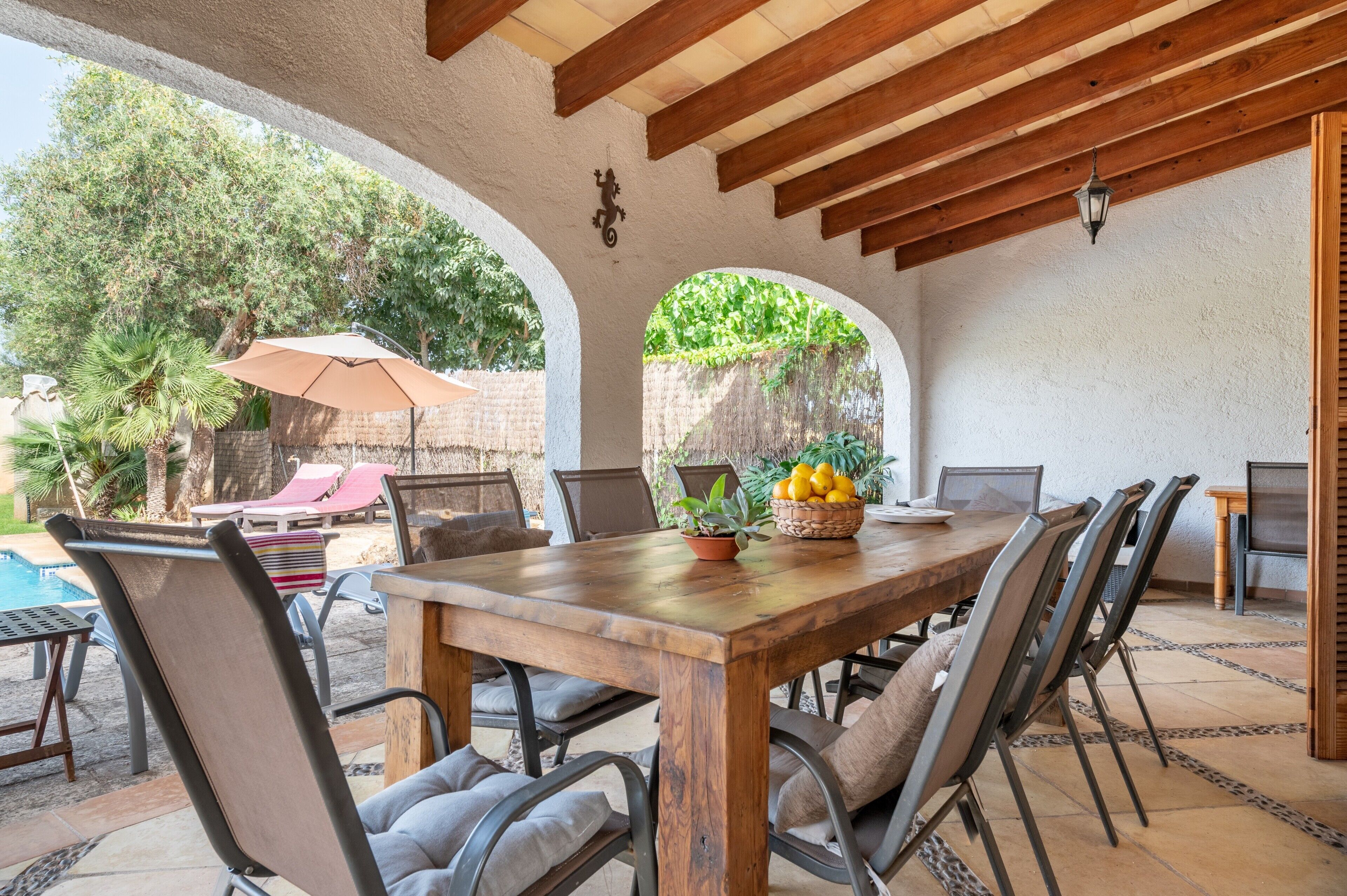 An outdoor patio with a wooden table, chairs, a pool, and umbrellas.