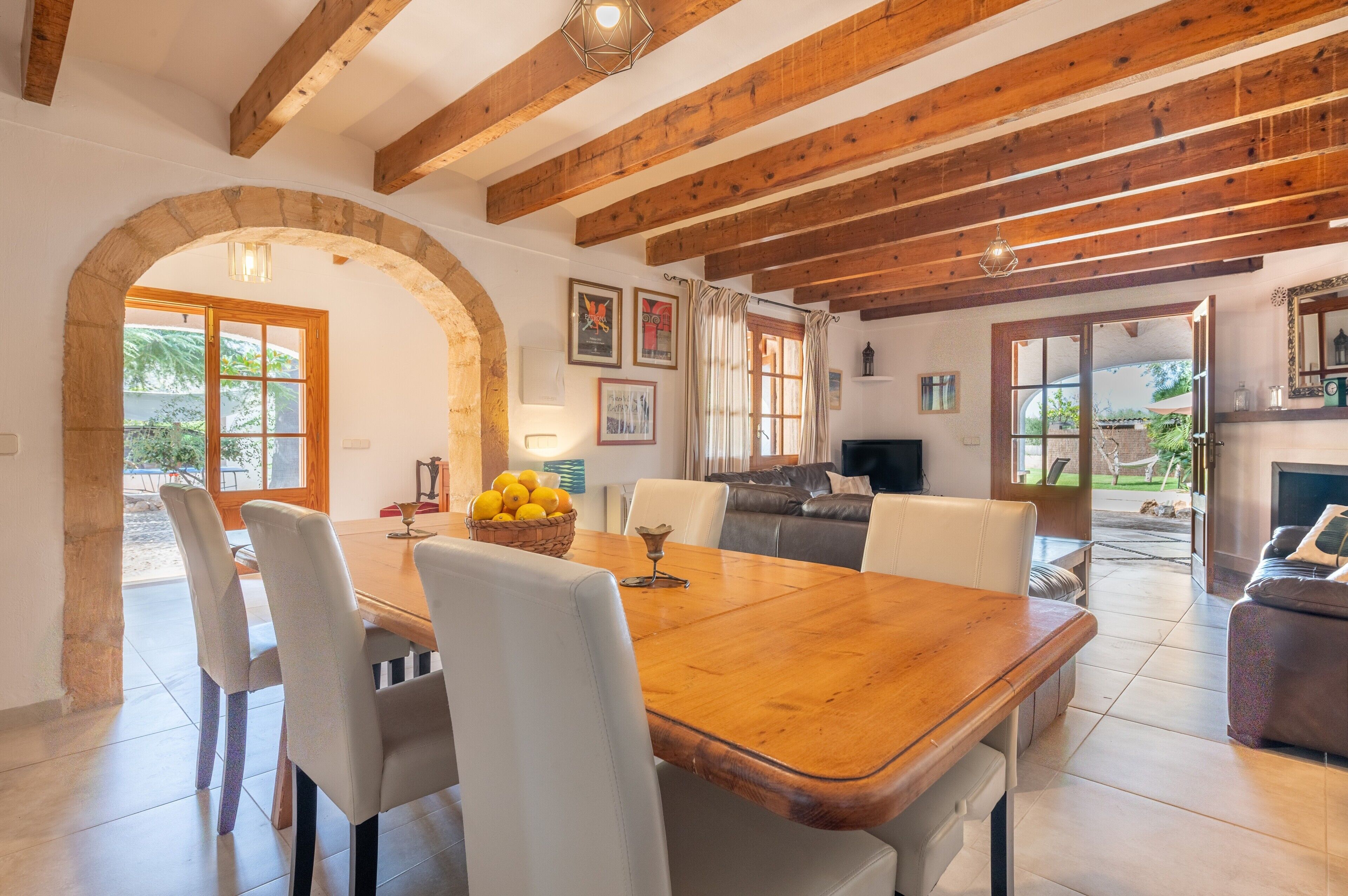 Un coin repas avec une table en bois, des chaises et un panier de fruits. On aperçoit une cheminée et un canapé au fond.