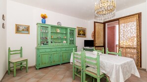 A dining area with a green cabinet, a table with a white tablecloth, and chairs. - Apartment  Azalea with Balcony & Wi-Fi (Valledoria)