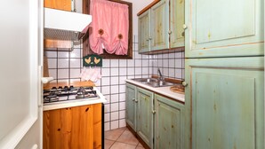 A kitchen with a gas stove, a window with pink curtains, and wooden cabinets. - Apartment  Azalea with Balcony & Wi-Fi (Valledoria)