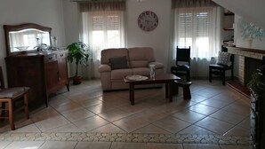 Un salon comprenant un canapé, une table basse, une cheminée, une horloge et un coin repas avec un buffet et des chaises.