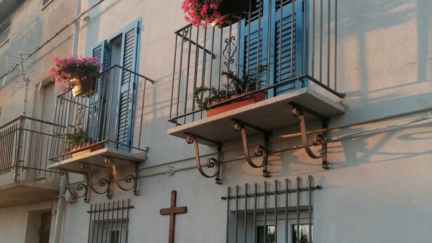 Un bâtiment doté de balcons, d’une fondation en pierre et d’une croix sur le mur.