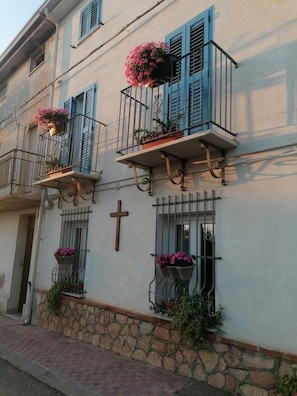 Ein Gebäude mit Balkonen, steinernen Fundament und einem Kreuz an der Wand.