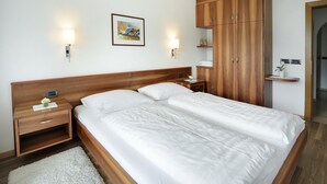 A double bed with a wooden headboard, bedside tables with lamps, a framed picture on the wall, and a wooden wardrobe.