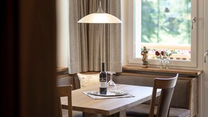 A dining table with a bottle and glass, cushioned chairs, a pendant light, a window with curtains, and a statue on the windowsill.