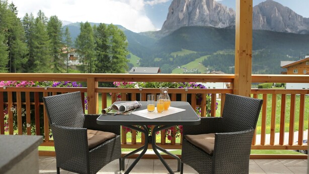 A balcony with wicker chairs, a table, and a view of mountains.