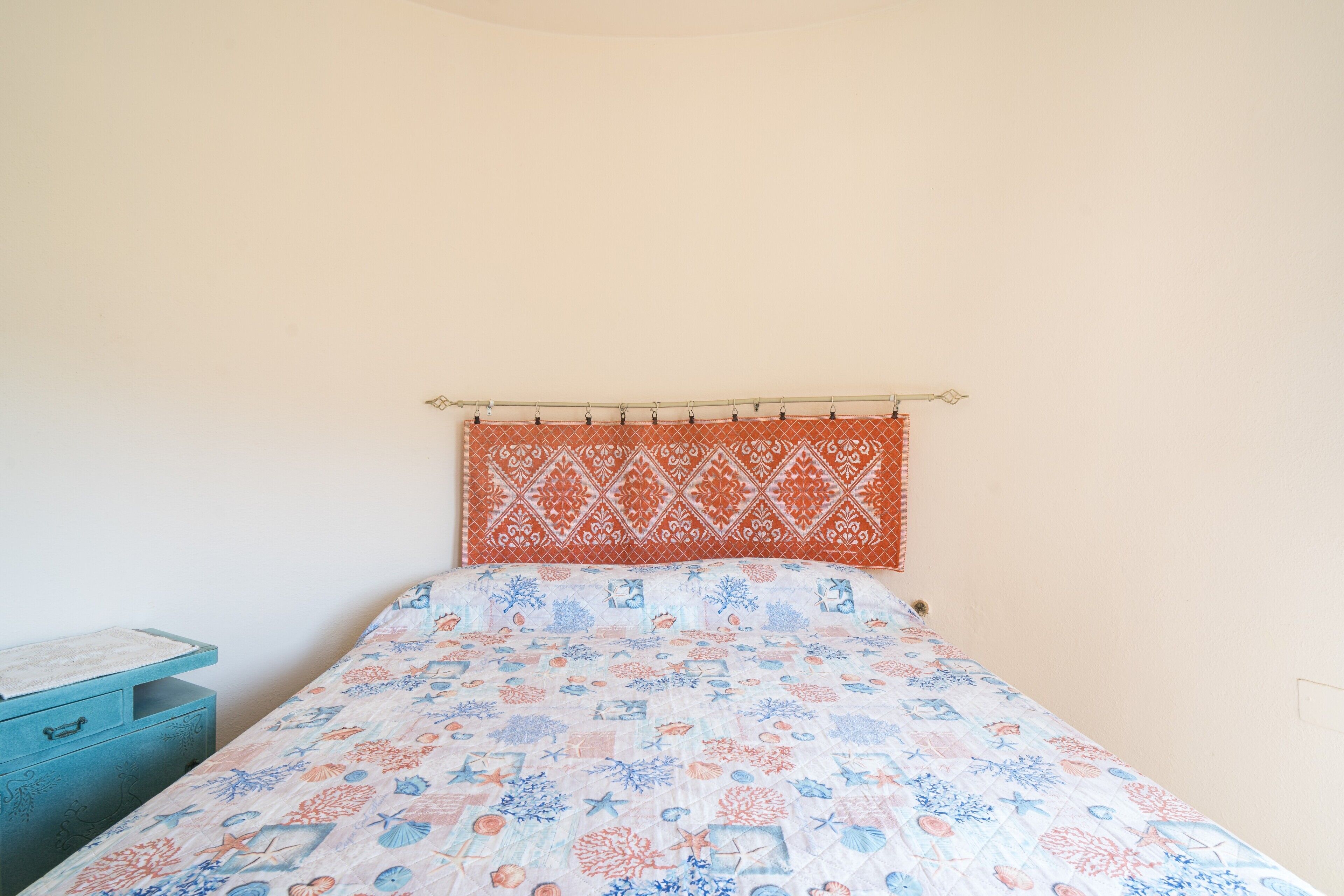 Un lit avec une couvre-lit à motifs, une table de chevet bleue et une tête de lit fixée au mur.
