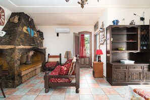 A room with a stone fireplace, a bed with red bedding, a wooden cabinet, and a tiled floor.