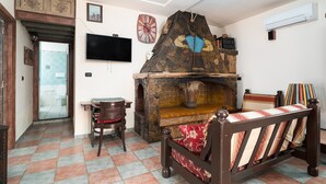 A room with a stone fireplace, a bed with patterned bedding, a television, and a tiled floor. - Holiday Home "Sa Burrida" with Garden, Covered Terrace & Fireplace (posada)