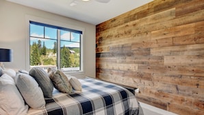Ein Schlafzimmer mit großem Fenster, einem Bett mit Karomuster-Bettdecke und einer Wand mit Holzpaneelen.