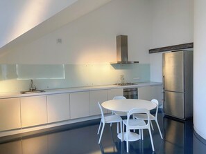 Cocina moderna con una isla central, sillas blancas, un refrigerador de acero inoxidable y un horno empotrado.