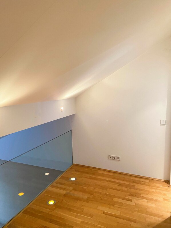 Una habitación con techo inclinado, suelo de madera y pared divisoria de vidrio.