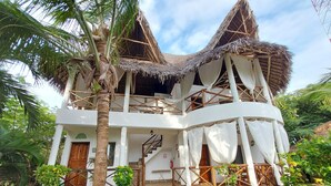 Un edificio de dos pisos con techo de paja, paredes blancas y una escalera de madera.