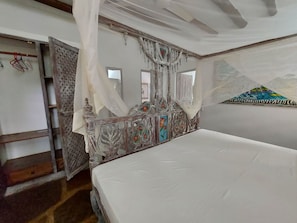 Quarto com cama, cabeceira de madeira com detalhes florais, dossel e painel na parede.