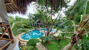 Una piscina rodeada de exuberante vegetación y una estructura con techo de paja.