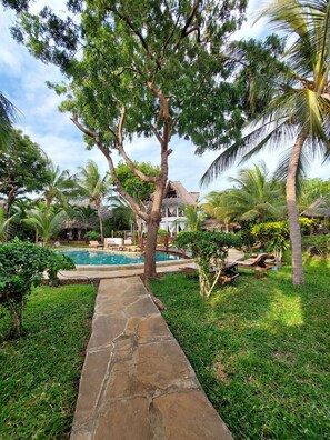 A stone pathway leading to a pool area surrounded by lush greenery and palm trees.