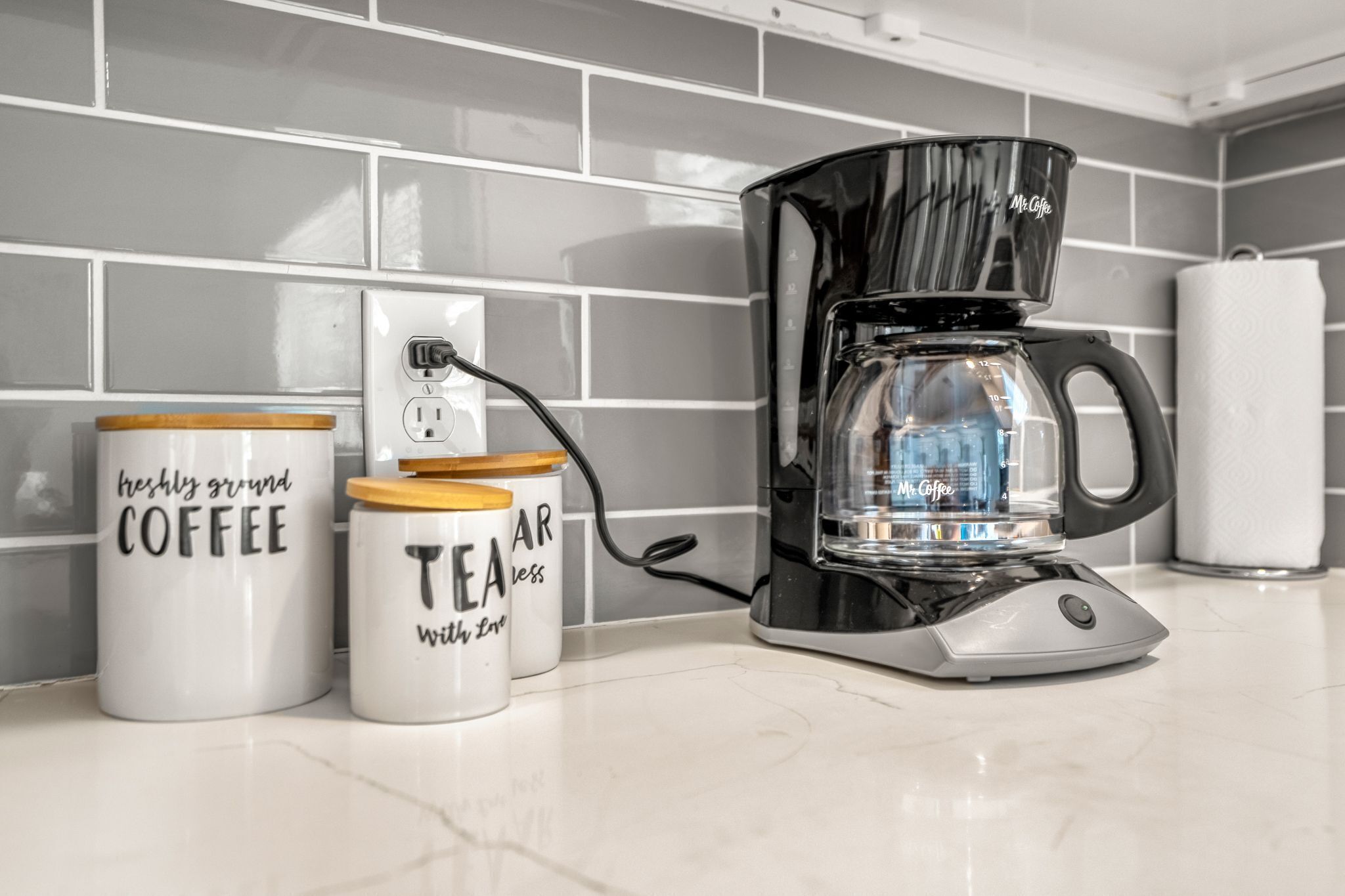 Une machine à café, deux récipients à café et une prise électrique sur un plan de travail de cuisine.