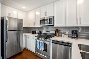 Uma cozinha moderna com eletrodomésticos de aço inoxidável, armários brancos e painel de azulejos.
