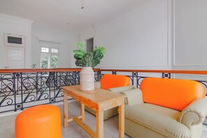 Un salon moderne avec un canapé beige, un fauteuil orange et une table en bois sur laquelle est posé un vase blanc.