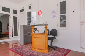 Ett receptionsområde med ett skrivbord, en stol, ett kylskåp och en mönstrad matta.