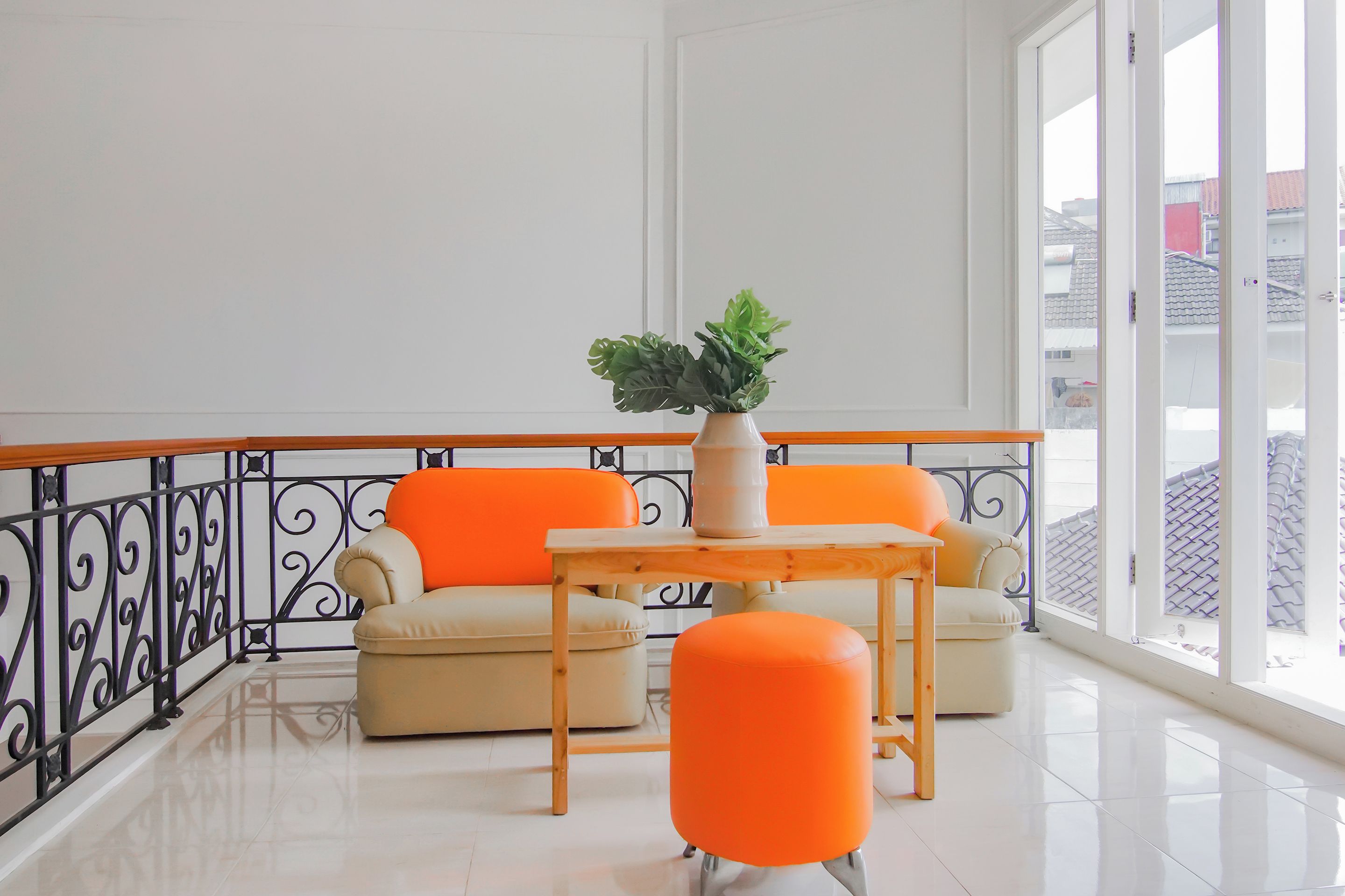 A balcony with a white railing, beige sofas, and an orange ottoman.