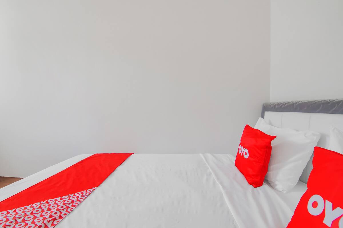 Un lit avec une literie blanche et des touches de rouge, notamment des coussins et une couverture.