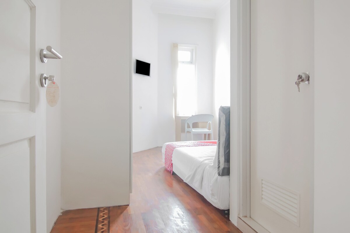 Un pasillo estrecho que conduce a un dormitorio con una cama, una silla y un televisor.