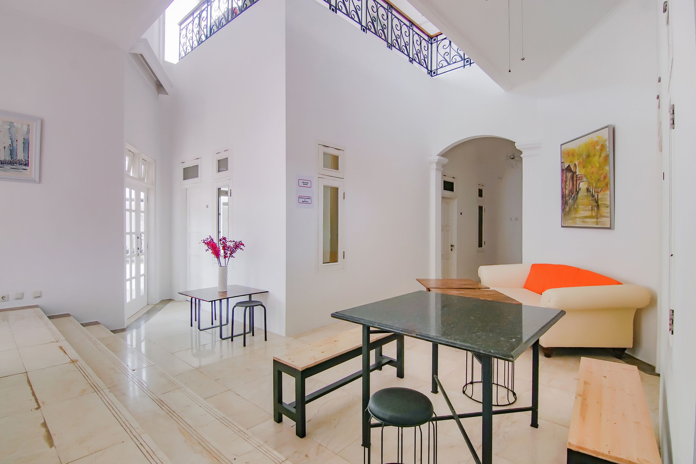 A spacious living area with a high ceiling, a dining table, a sofa, and a staircase leading to an upper level.