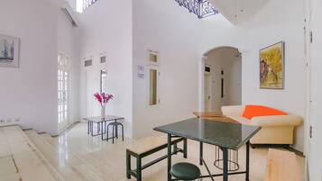 A spacious living area with a high ceiling, a dining table, a sofa, and a staircase leading to an upper level.
