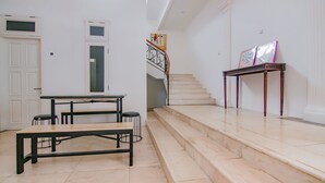 Un interior espacioso con una escalera, un comedor con mesa y bancos, y una pequeña mesa con cuadros enmarcados.