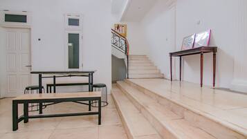 A spacious interior with a staircase, a dining area with a table and benches, and a small table with framed pictures.