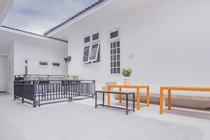 Un bâtiment blanc avec un toit recouvert de tuiles, un balcon doté d’une rambarde en métal et deux tables ornées de plantes en pot.