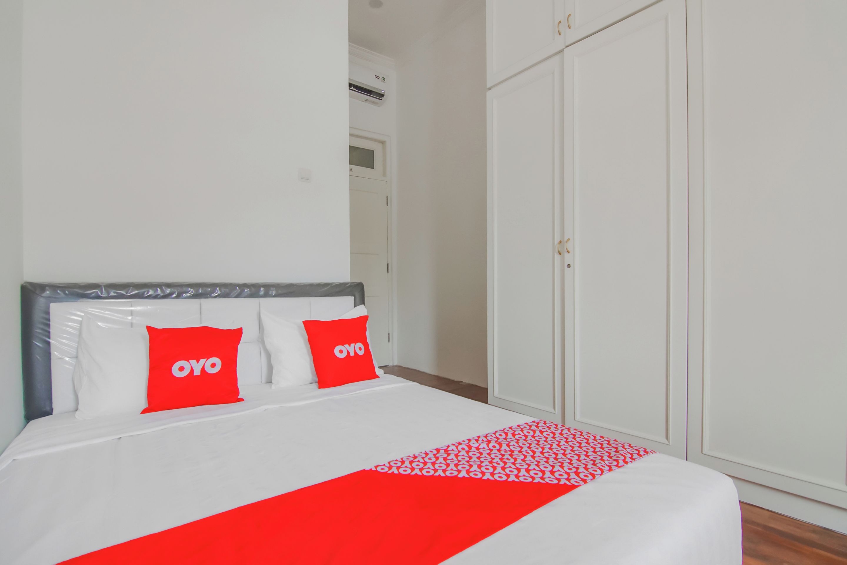 Een bed met witte beddengoed en rode accenten, een kledingkast en een deur met een handgreep.