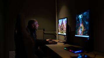 A person seated at a table with two monitors displaying video games.