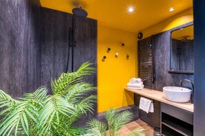 A modern bathroom with a yellow accent wall, a large mirror, a sink, and a shower area.