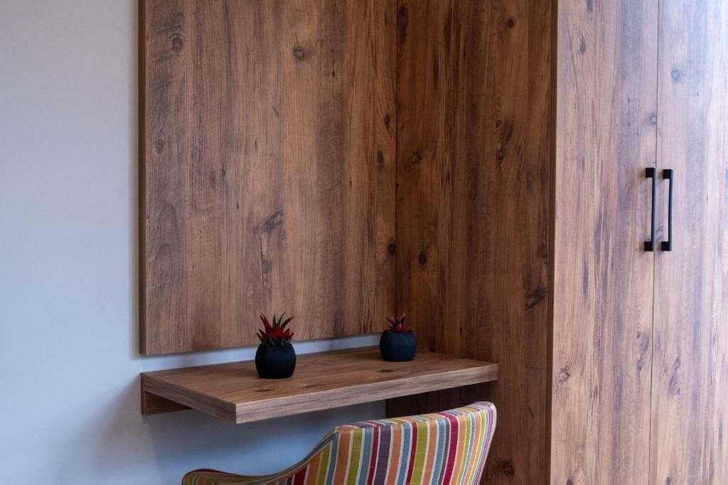 A wooden wardrobe with a shelf, two small potted plants, and a striped cushion.