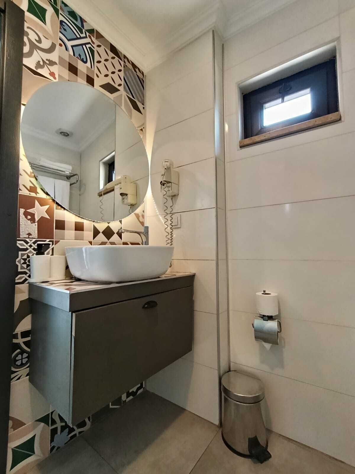 A bathroom with a white sink, a mirror, a toilet paper holder, and a trash can.