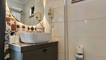 A bathroom with a white sink, a mirror, a toilet paper holder, and a trash can.