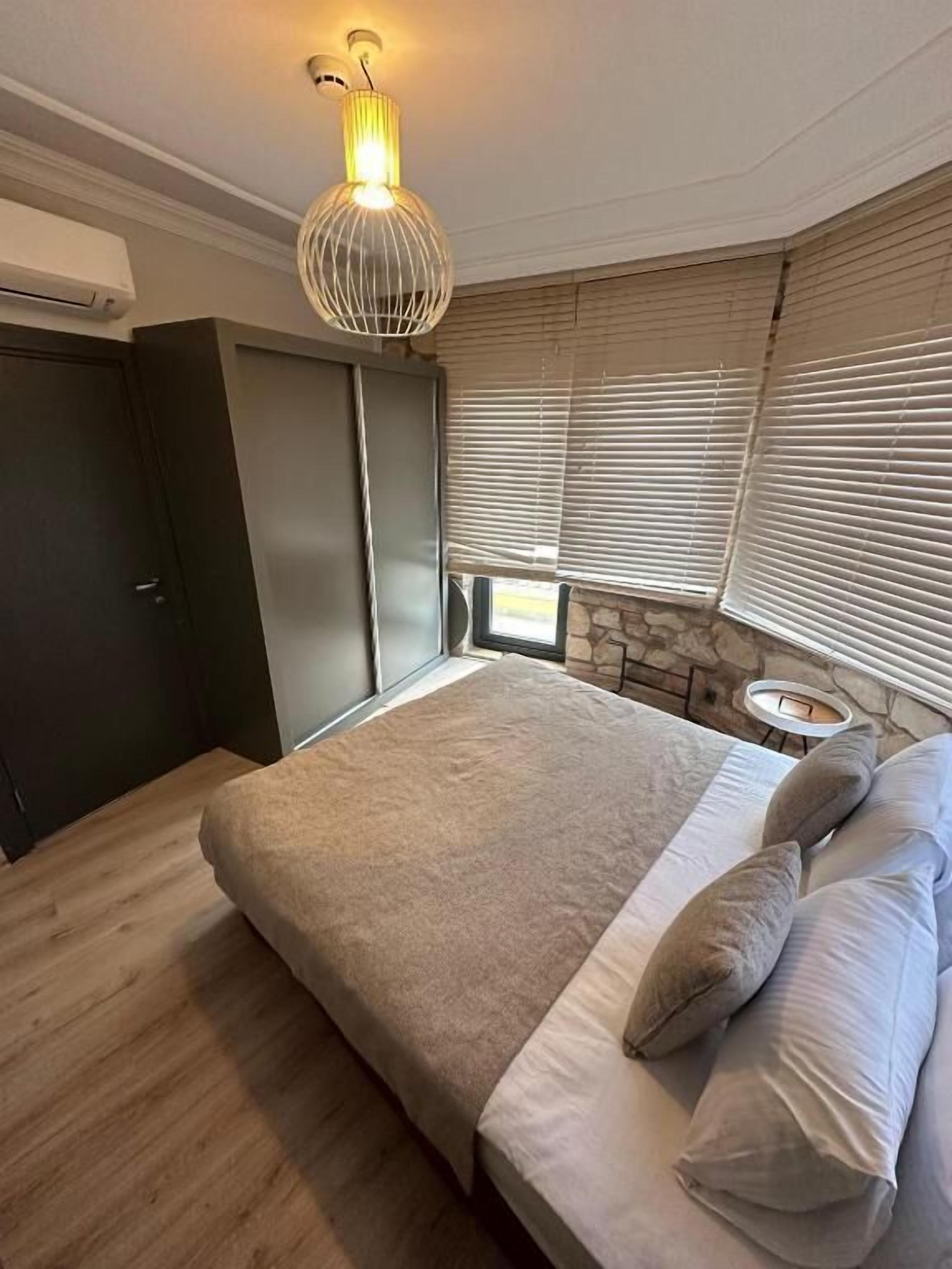 Un dormitorio con cama, armario, ventana con persianas y una lámpara fijada a la pared.