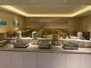 L'intérieur d'un restaurant, avec des tables, des chaises et un espace buffet.