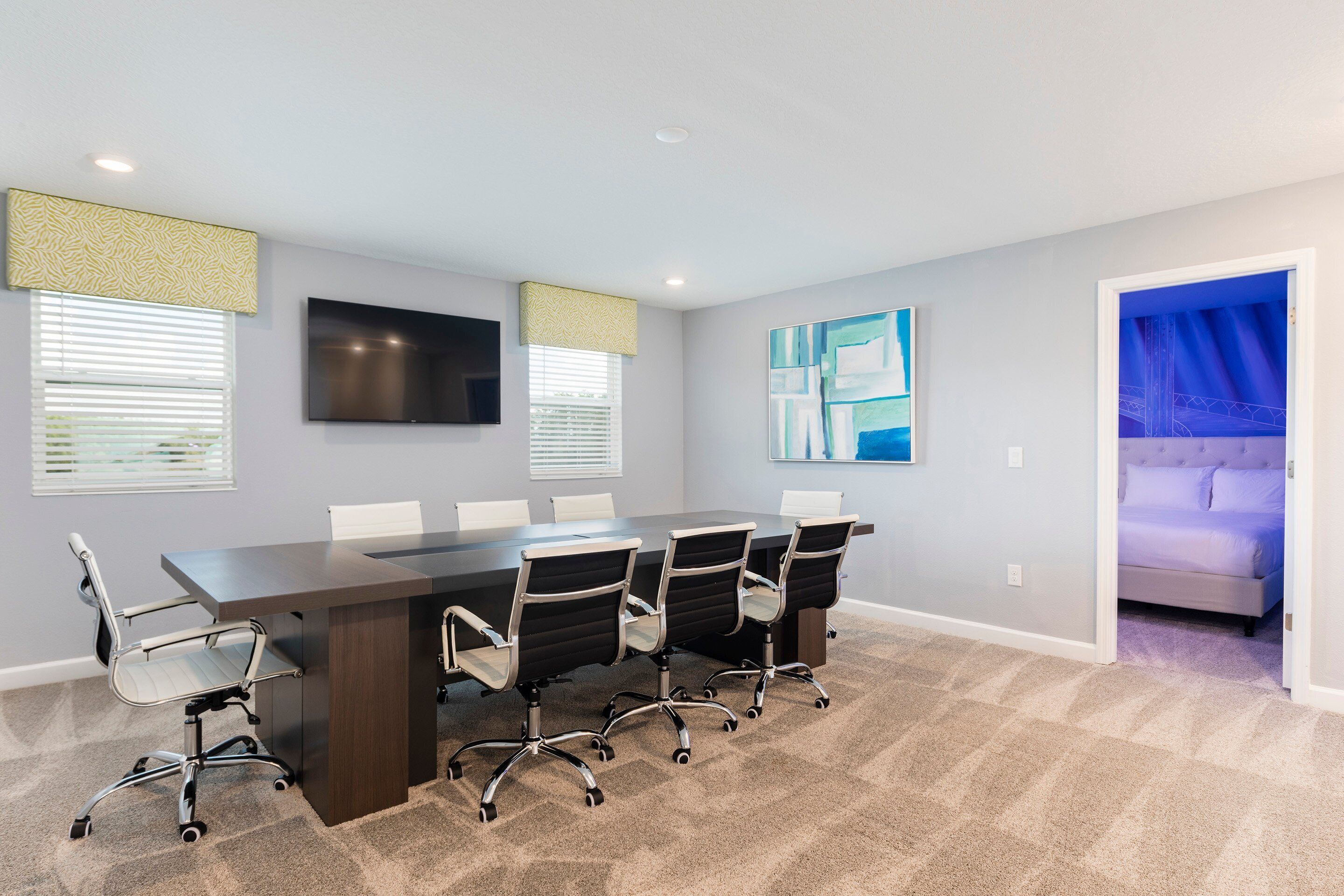 A conference room with a long table, four chairs, a flat-screen TV, and artwork on the walls.