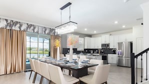 A modern kitchen with white cabinets, stainless steel appliances, and a dining area with a glass table and white chairs. - Lakeview Luxury Villa with Everything! (Kissimmee)