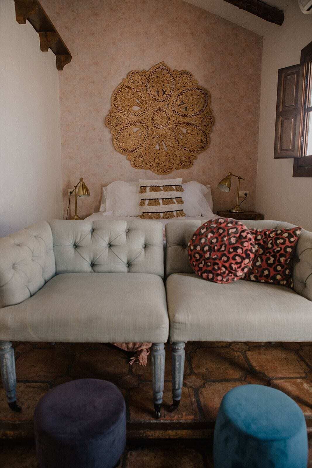 Ein Zimmer mit einem hellen Sofa, einem gemusterten Zierkissen und einem Wandbild.
