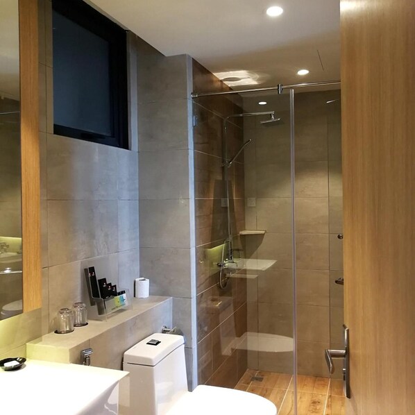 A modern bathroom with a glass-enclosed shower, a white sink, and a mirror. - The Granite Luxury Hotel (George Town)