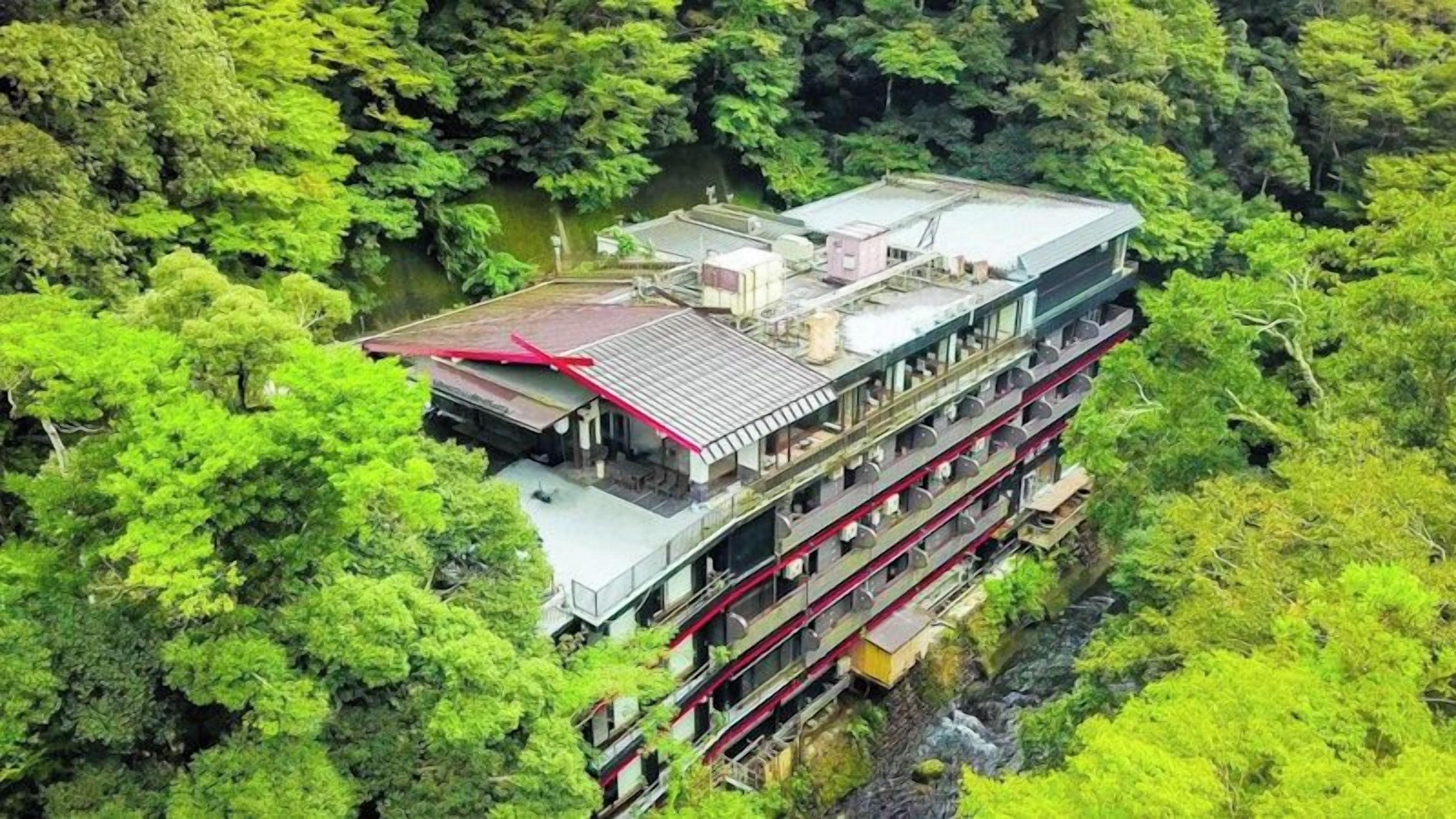Un edificio a più piani con tetto rosso, immerso in un fitto fogliame verde.