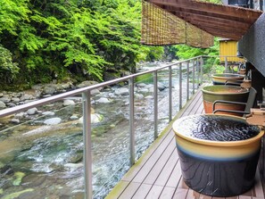 Une terrasse en bois surplombant une rivière parsemée de rochers, le tout entouré de verdure.