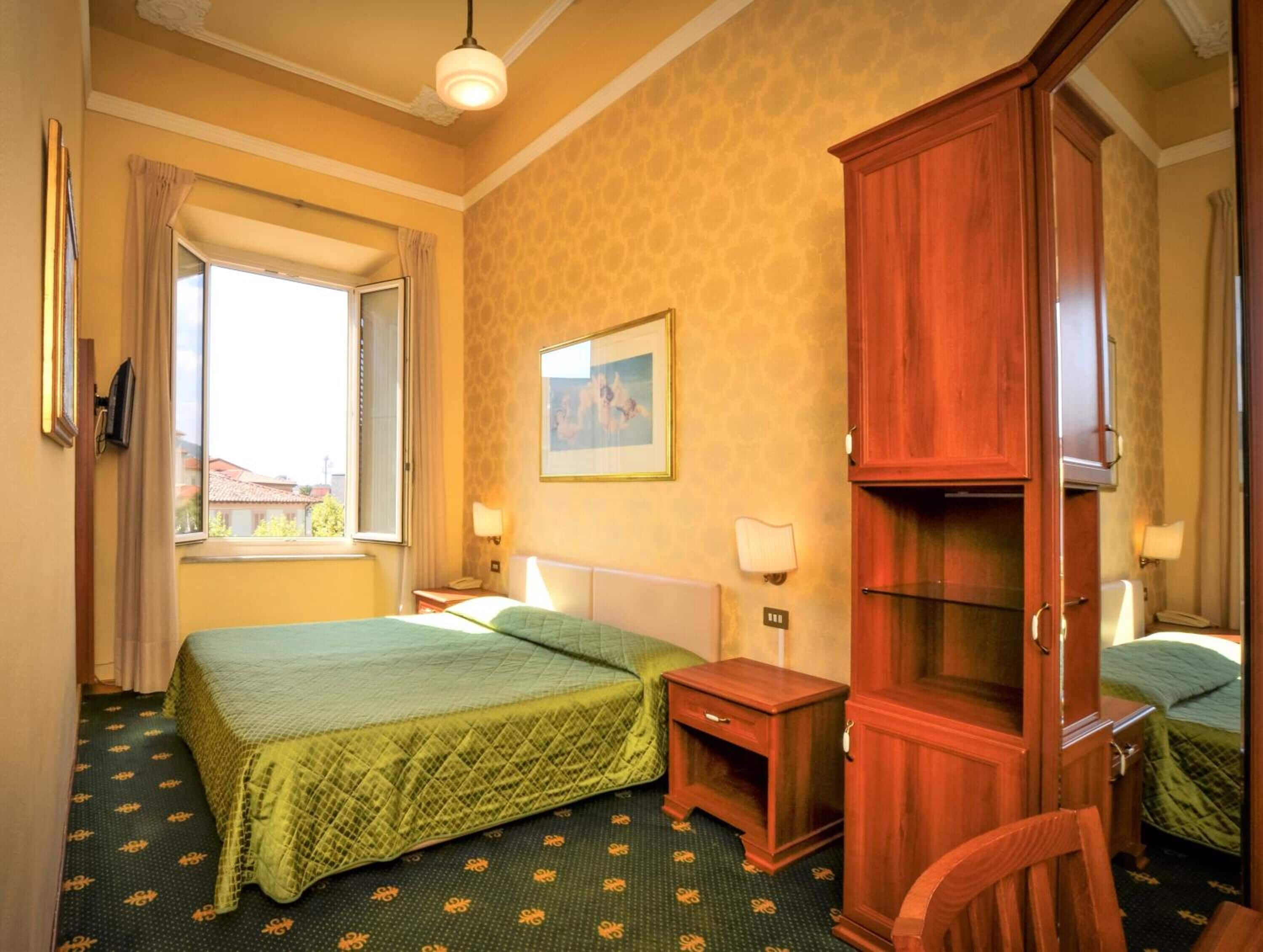 A hotel room with two beds, a wooden wardrobe, a desk, a chair, and a window with curtains.