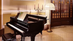 A grand piano in a well-lit room with a framed portrait above it, a candelabra with candles, and a traditional wooden door.