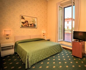 Habitación de hotel con cama, dos lámparas de noche, un televisor, ventana con vista y un cuadro en la pared.